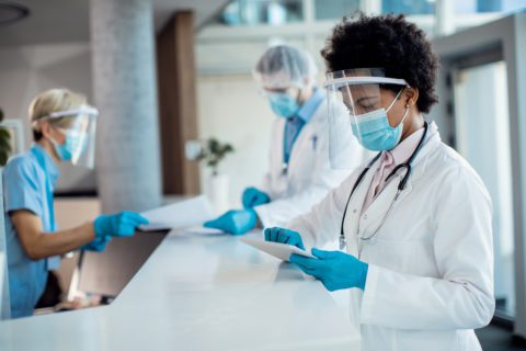 African American doctor working on touchpad at reception desk in the hospital during coronavirus pandemic.