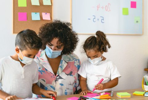 Teacher with children wearing face mask in preschool classroom during corona virus pandemic - Healthcare and education concept