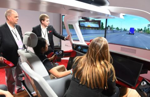 A group of individuals trying a driving simulator at the Detroit Auto Show