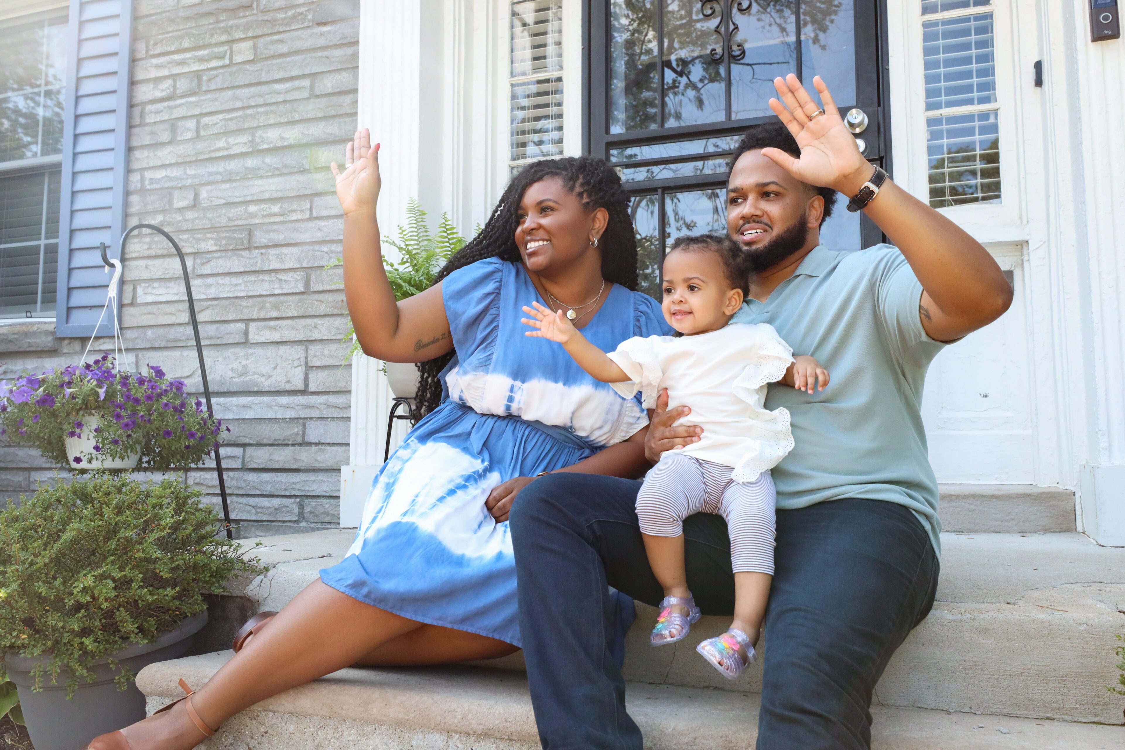 A Black couple holding their child while smiling and waving