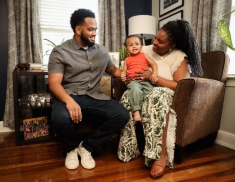 A Black man and woman holding their child and smiling