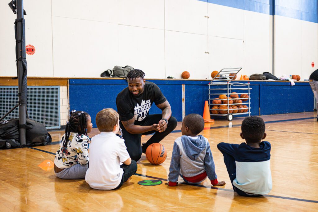 An adult male teaching young children how to play basketball