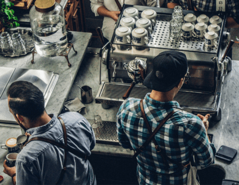 Small Business Index Report image featuring a small business owner and employee standing behind coffee bar preparing coffee for customers